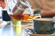 Aus einer Glaskanne wird Schwarztee in eine Steingut-Tasse gegossen schwarztee